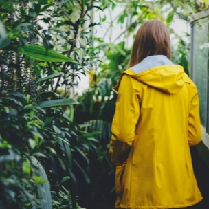 A woman in a yellow raincoat turned away from you, looking at the greenery in the background.