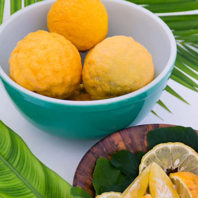  3 ladoos in a bowl at the top left corner, with a plate of lemons in the bottom right corner and a green leaf in the other two corners.