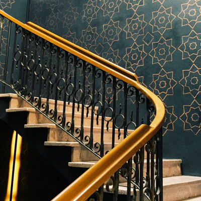 A staircase with black rails and wooden colored handle. The wallpaper is green with a gold colored star pattern.